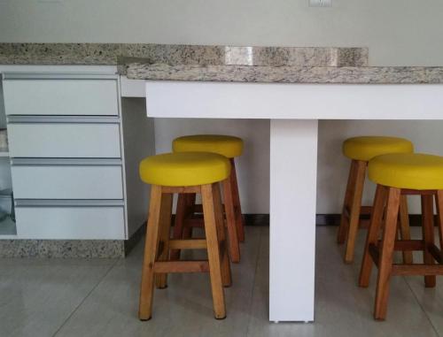 a counter with four yellow bar stools under it at Residencial Franca Garopaba in Garopaba