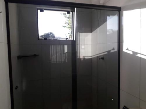a glass shower door in a bathroom with a window at Residencial Franca Garopaba in Garopaba