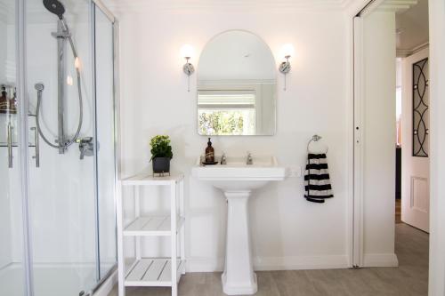 bagno bianco con lavandino e specchio di White Cottage a Matakana