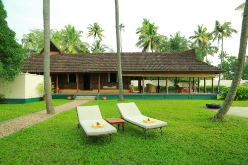two white chairs and a house in the grass at Vismaya by Moksha Stays in Turavūr