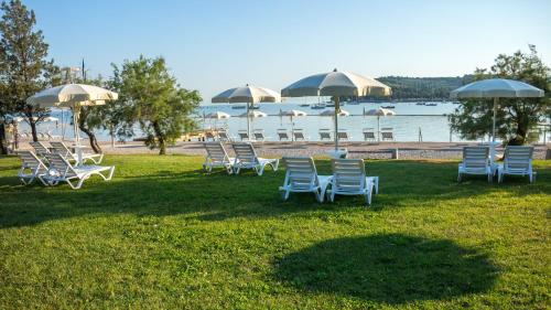 a group of chairs and umbrellas on the grass near the water at Bioenergy Resort Salinera Apartments in Strunjan