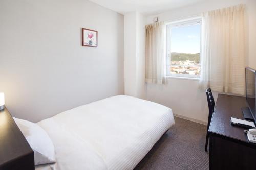 a bedroom with a bed and a desk and a window at Hotel Mystays Nayoro in Nayoro