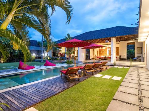 a pool with chairs and umbrellas next to a house at Villa Arte in Seminyak
