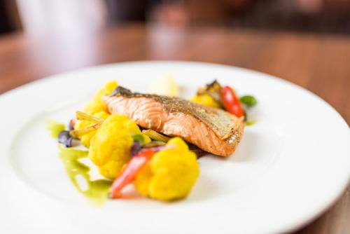 a white plate with a piece of fish and vegetables at Hotel Kaskáda in Kuřim