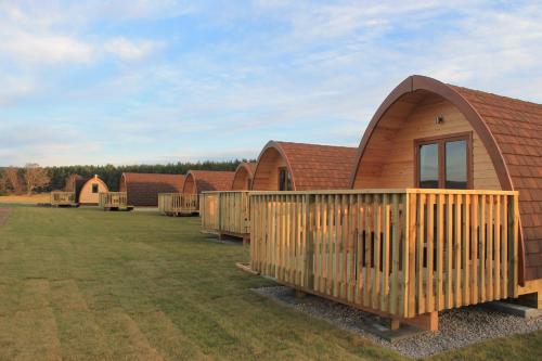 a home with a wooden deck on a grass field at Evelix Pods Dornoch in Dornoch