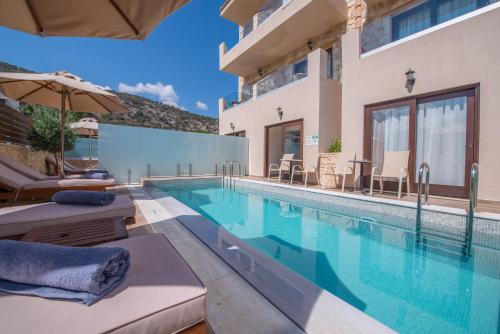 a swimming pool with chairs and an umbrella next to a house at Cactus Royal Spa & Resort Adults Only in Stalida