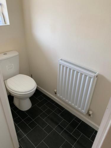 ein Badezimmer mit einem weißen WC und einem schwarzen Fliesenboden in der Unterkunft Cosy Corner House in Kettering
