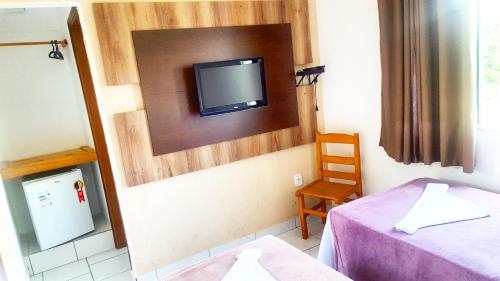 a room with a tv on a wall with a bed and a chair at Chalé Alto da Serra SP in Serra Negra