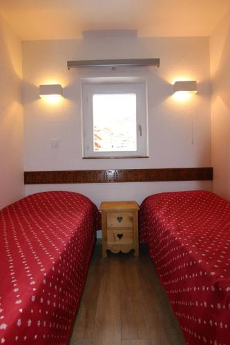 two beds in a room with red sheets and a window at Altineige Appartements VTI in Val Thorens