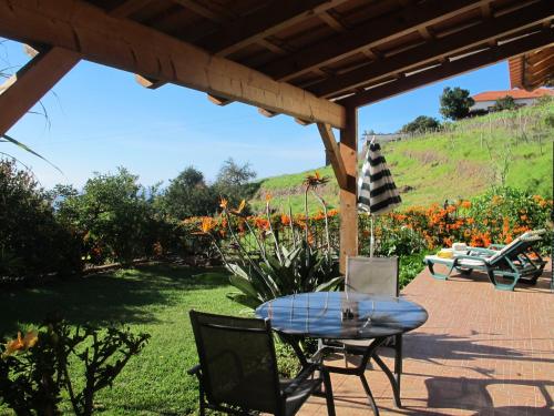 eine Terrasse mit einem Tisch und Stühlen unter einem Dach in der Unterkunft Blooming Botanic Houses in Estreito da Calheta