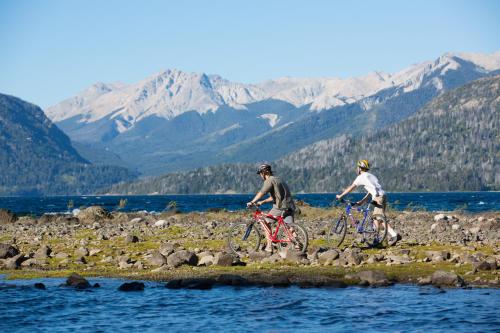 two people riding bikes on a rocky beach near the water at Hostería Isla Victoria Lodge in Isla Victoria