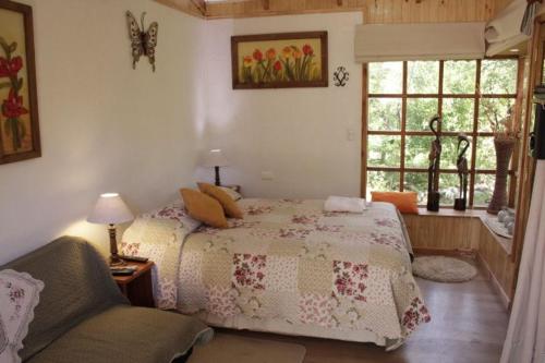 a bedroom with a bed and a chair and a window at Complejo Cabañas Pétalos in Villarrica