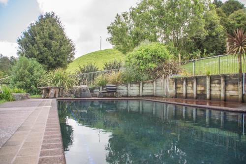 a swimming pool in a garden with a hill in the background at JunoHall Backpackers in Waitomo Caves