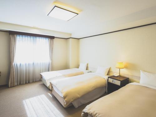 軽井沢町にある ホテル軽井沢エレガンスのベッド3台と窓が備わるホテルルームです。