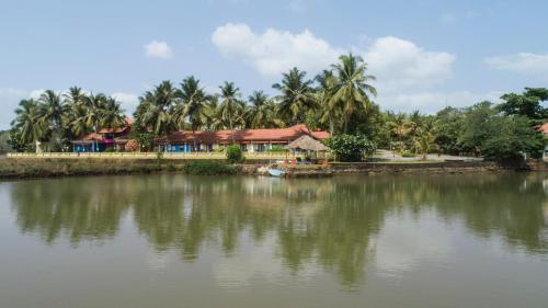 a house by a body of water with palm trees at Mercure Goa Devaaya Resort in Old Goa