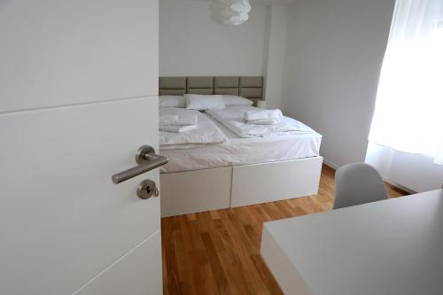 a white bedroom with a bed and a chair at HOME APARTMANI I SOBE in Osijek