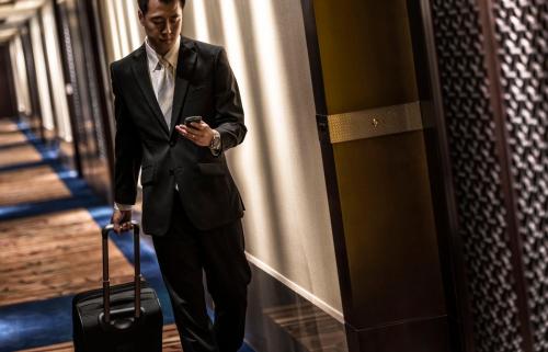 a man in a suit holding a suitcase and looking at his cell phone at Four Seasons Hotel Beijing in Beijing