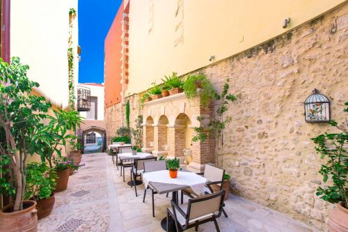 un patio con mesas y sillas y una pared de piedra. en Casa Moazzo Suites and Apartments en Rethymno