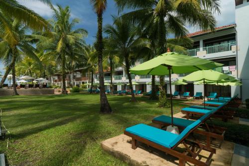 a row of beach chairs with umbrellas and palm trees at The Briza Beach Resort, Khao Lak SHA Extra Plus in Khao Lak