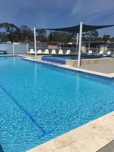 a large blue swimming pool with chairs in the background at Lakeside Cabins & Holiday Village in Sussex inlet