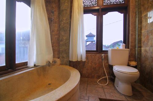 a bathroom with a tub and a toilet and windows at Hibiscus Cottages in Ubud
