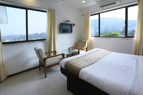 a bedroom with a bed and two chairs and windows at Sunrise Hill Resort in Khandala