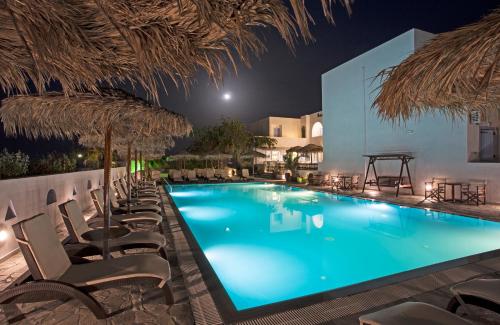 una piscina por la noche con sillas y sombrillas en Alexandra Hotel en Kamari