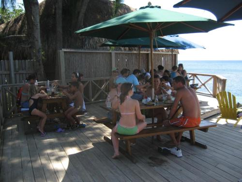 a group of people sitting at tables on the beach at Las Rocas Resort and Dive Center in West Bay