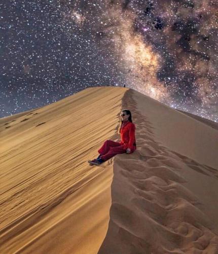 a woman sitting on a sand dune under the stars at Camp Sahara Holidays in Mhamid
