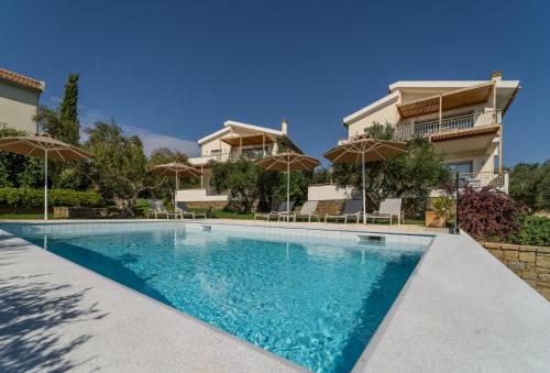 a swimming pool in front of a house with umbrellas at Abelia Luxurious Villas in Finikounta