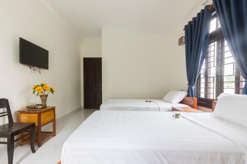 two beds in a room with a tv and a window at New Destination Hoi An in Hoi An
