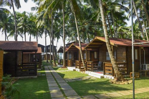 a row of wooden cottages with palm trees at Agonda Paradise in Agonda