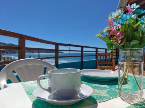 a table with a coffee cup and a vase of flowers at Residencial Vila do Sol, Apartamentos com pé na areia in Bombinhas
