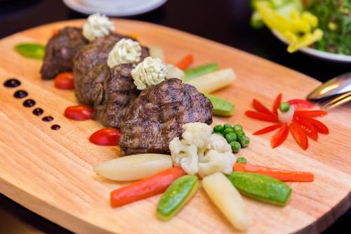 a wooden cutting board with meat and vegetables on it at Holiday Jazan Hotel in Jazan