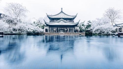 a building with a building over a body of water at Four Seasons Hotel Hangzhou at West Lake in Hangzhou