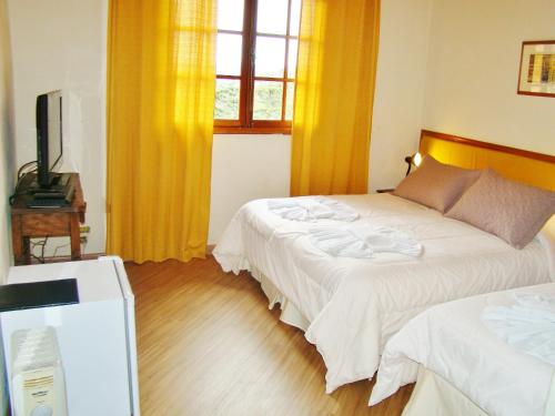 a bedroom with two beds with yellow curtains and a television at Alpenhaus Pousada in Campos do Jordão