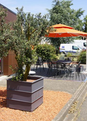a potted tree in a planter with a table and umbrella at ibis Le Mans Est Pontlieue in Le Mans