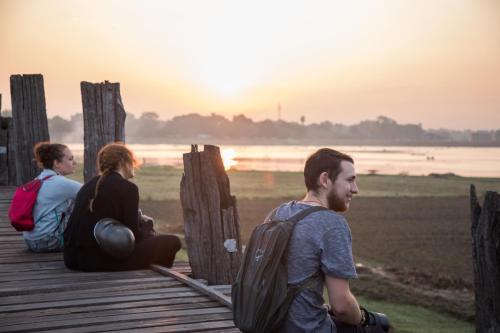 three people sitting on a pier looking at the sunset at Ostello Bello Mandalay in Mandalay