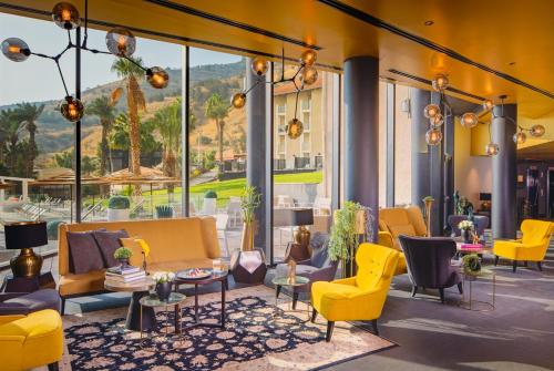 a lobby with yellow chairs and tables and windows at Hotel Lake House Kinneret in Tiberias