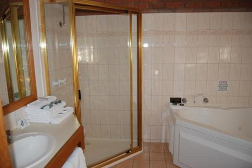 a bathroom with a shower and a sink and a tub at Sportslander Motor Inn in Moama