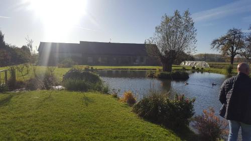 un hombre parado junto a un estanque frente a un edificio en chambre coin nature en Fromelles