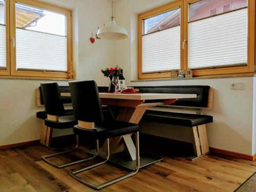 a dining room table with black chairs and windows at Apart Alpenrose in Schwendau