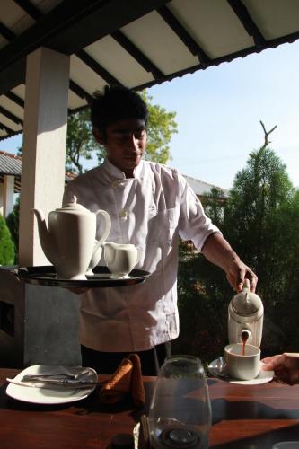 a man holding a tray with cups on a table at Flower Garden Lake Resort in Tissamaharama