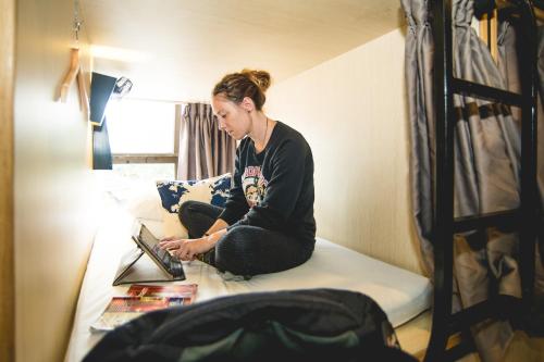 a woman sitting on a bed using a laptop at Traveller Bunker Hostel in Cameron Highlands