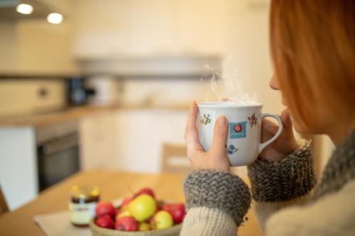 a woman holding a cup of coffee with a bowl of fruit at Kronhofer – Apartments & Erlebnis-Imkerei in Hermagor