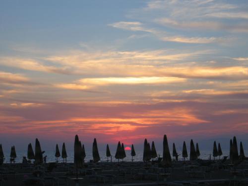 a group of closed umbrellas in front of a sunset at Oltremare Appartamenti in Principina a Mare