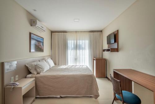 Schlafzimmer mit einem Bett, einem Schreibtisch und einem Fenster in der Unterkunft Residencial Onda Azul in Bombinhas