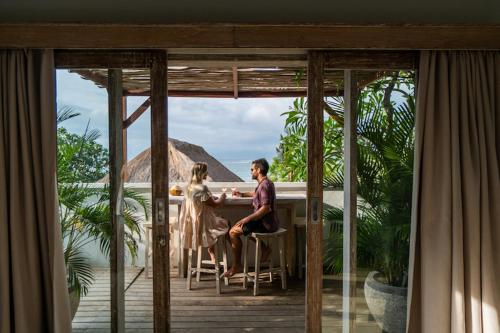 a man and woman sitting at a table on a porch at Tenang Villas in Nusa Lembongan