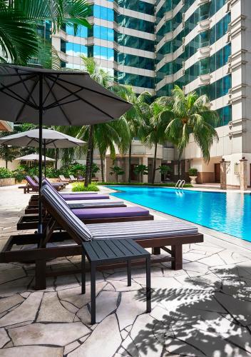a pool with two lounge chairs and an umbrella at Pullman Kuala Lumpur City Centre Hotel & Residences in Kuala Lumpur