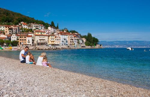 a man and two children sitting on a rocky beach at Hotel Marina - Liburnia in Mošćenička Draga
